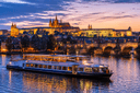 Prague sightseeing evening cruise on the Vltava River with Charles Bridge and Prague Castle illuminated at sunset.